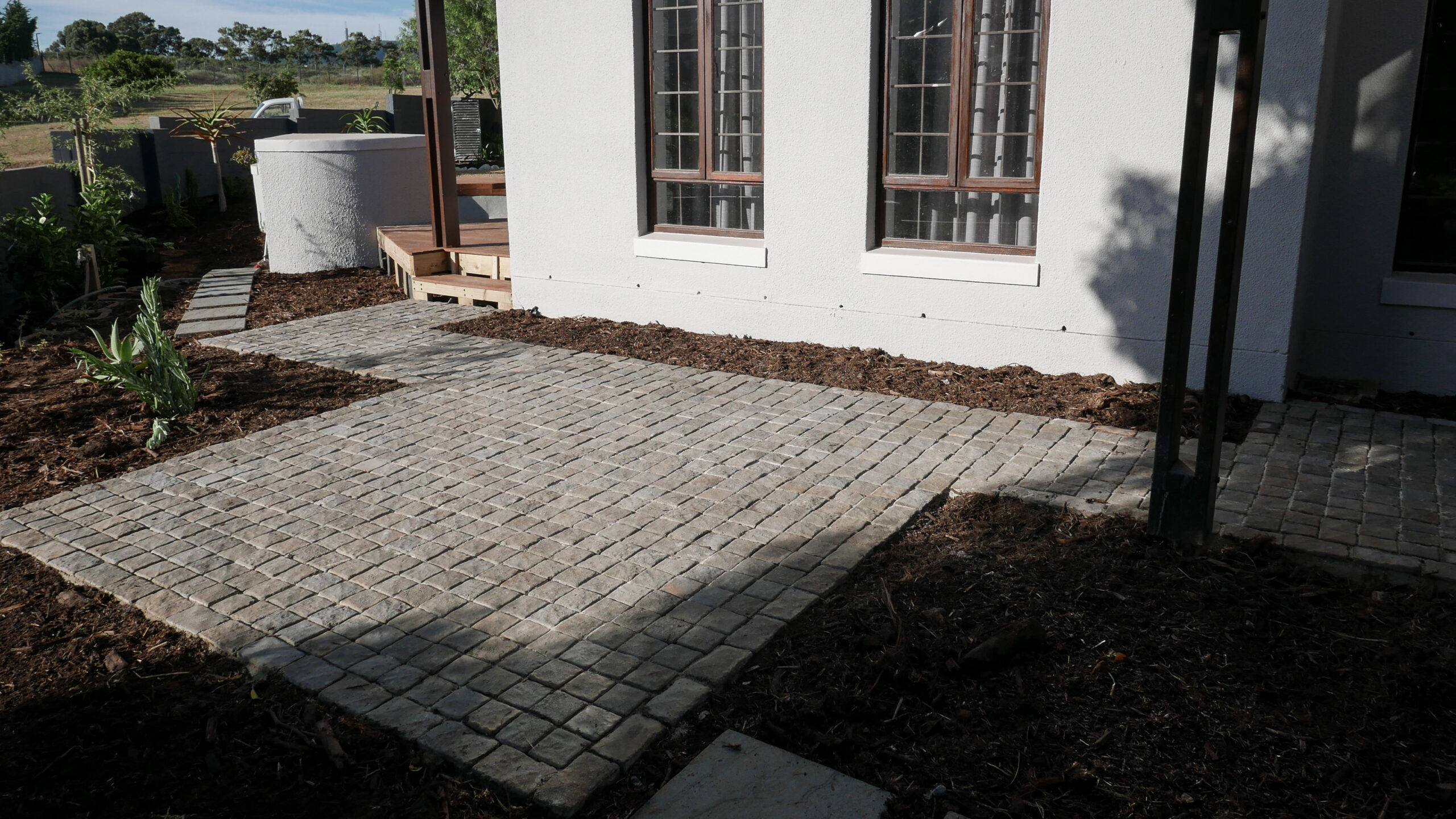 horizon-paving-project-landskroon-reclaimed-cobbles-hero Patio paving in Van Riebeeckshof Cape Town with reclaimed charcoal cobblestones and sandstone slabs forming an intimate courtyard beneath a tree